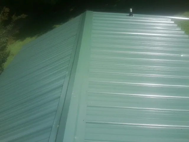 New green metal panels meeting at the ridge of a roof — Flat Roof Repair work by our crew in Shrewsbury