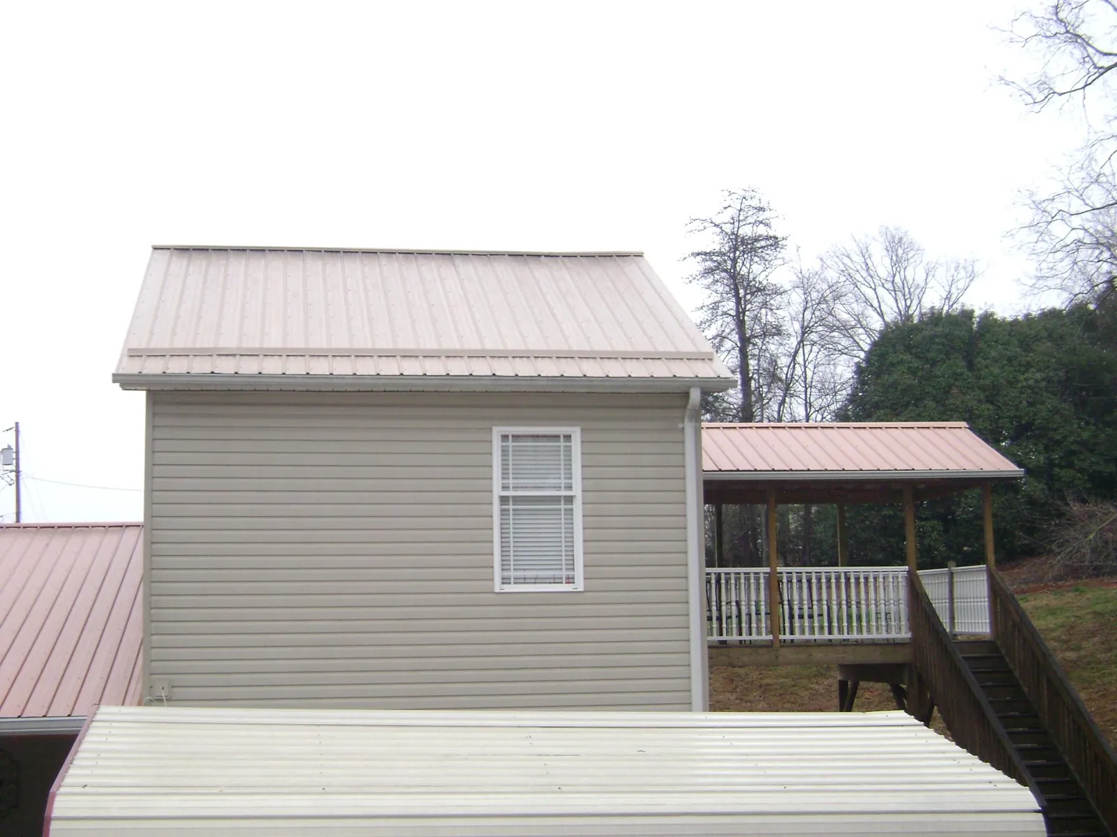 Tan metal roofs on a two story addition and attached porch, from a Roof Replacement job in Shrewsbury